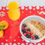 A vibrant breakfast setup with fruits, nuts, and juice on a Christmas-themed mat.